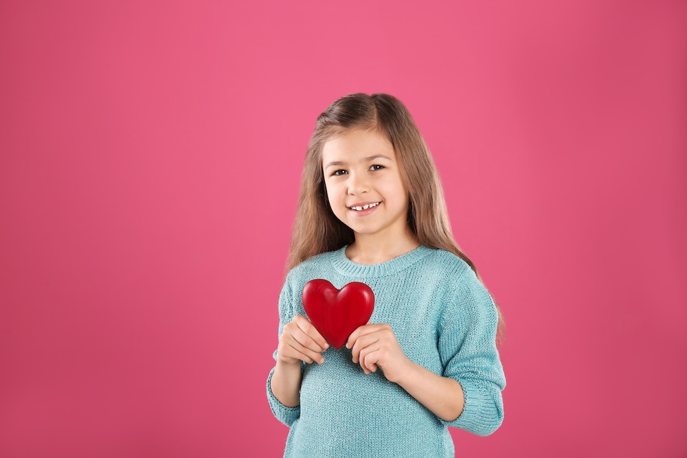 Child holding a red heart against a pink background to represent heart-healthy habits and pediatric wellness