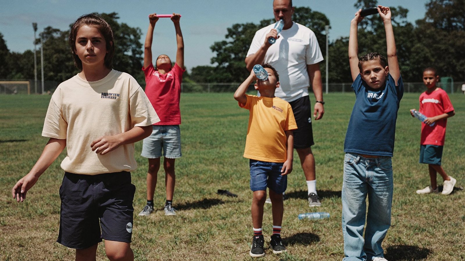 Young athletes stretching and drinking water on a sunny sports field
